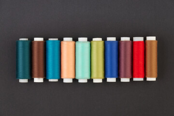 Panoramic detailed view of multi-colored spools of thread on a black background.