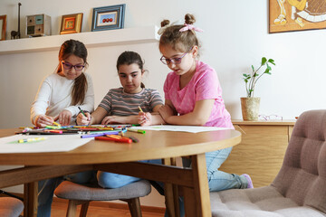 	 A group of school girls draw with color pencils. They're sitting at the table in the living room and having fun.	