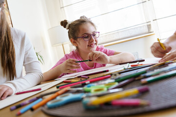 	 A group of school girls draw with color pencils. They're sitting at the table in the living room and having fun.	