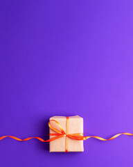 Brown paper gift box with an orange ribbon bow on purple violet background at the bottom with copy space. Flat lay father and mother day happy birthday and presents concept