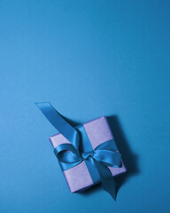 Brown paper gift box with a dark blue satin ribbon bow on blue background at the bottom with copy space. Flat lay father and mother day and presents concept