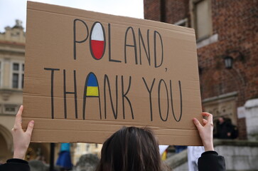 Poster with slogan POLAND THANK YOU and painted flags of Poland and Ukraine holds by woman while...