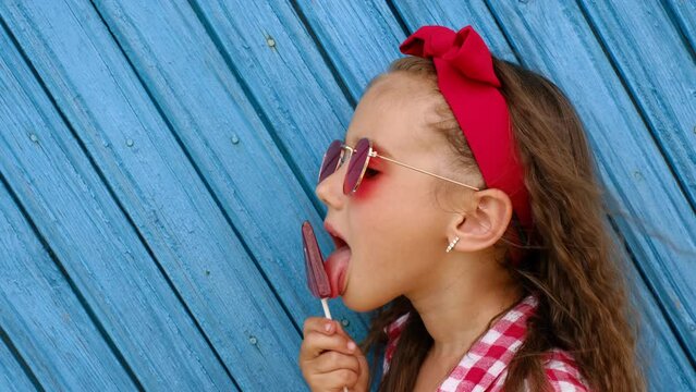 The girl eats a sweet lollipop, licking and enjoying the candy. Harm from the use of sugars. Risk Of Developing diabetes - Powered by Adobe