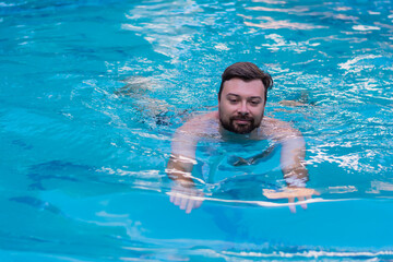 Lifestyle vacation handsome man with a beard on vacation swims in the blue pool resort