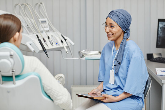 Portrait of Muslim young woman wearing medical uniform while consulting patient in modern dental clinic
