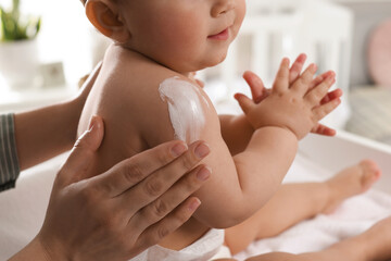 Mother applying body cream on her little baby at home, closeup - obrazy, fototapety, plakaty
