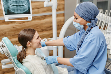 Side view portrait of young female dentist wearing mask while preparing patient for procedure in...