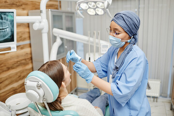 Portrait of Muslim young woman working as dentist and examining patient sitting in chair at dental...