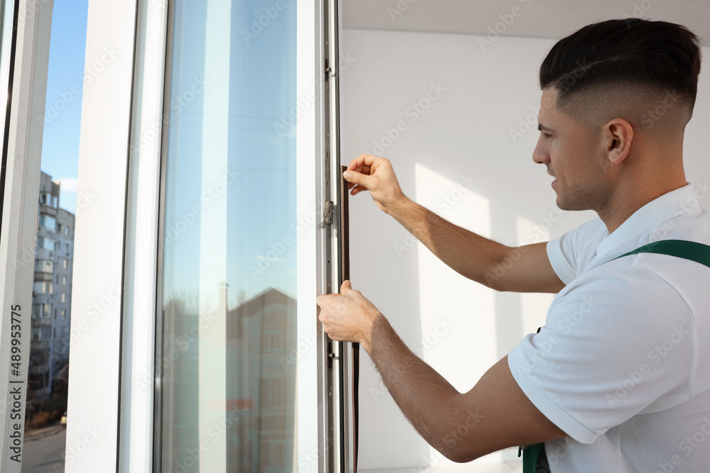 Wall mural Worker putting rubber draught strip onto window indoors