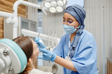 Waist up portrait of young female dentist working with patient sitting in dental chair at clinic