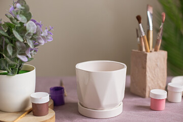 A still life with a white ceramic flower pot stands on a table on purple kraft paper