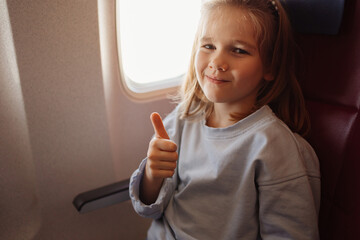a funny little girl shows the class with thumb in an airplane seat by the window