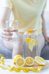 Healthy drink - water with lemon. Female drinking from the glass on background. Concept of clean eating, low calories, weight loss, dieting. Natural organic morning beverage
