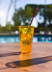A glass with a cocktail on the background of blue water in the pool. Sunny hot day.