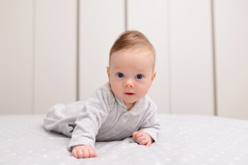 Naklejka premium Portrait of cute smiling happy baby boy crawling on bed on the white blanket in bedroom.