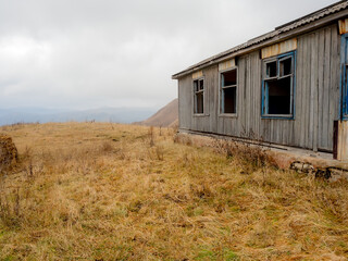 Fototapeta na wymiar An old abandoned wooden house in an autumn highland field under low hanging thick clouds