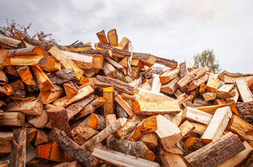 A pile of split firewood for heating a house, in an open space, close-up, against a blue cloudy sky.