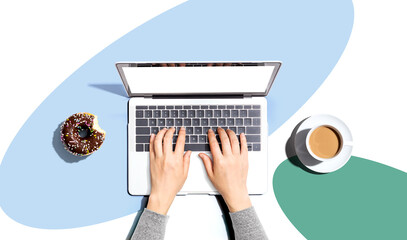 Person using a laptop computer with a donut and a cup of coffee - Flat lay