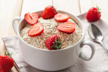 Oat muesli and fresh strawberries on wooden background. Bowl of oatmeal and berries