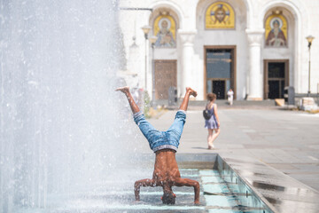 Gipsy boy performs stunts standing on head and cool off from the summer heat in the fountain water...