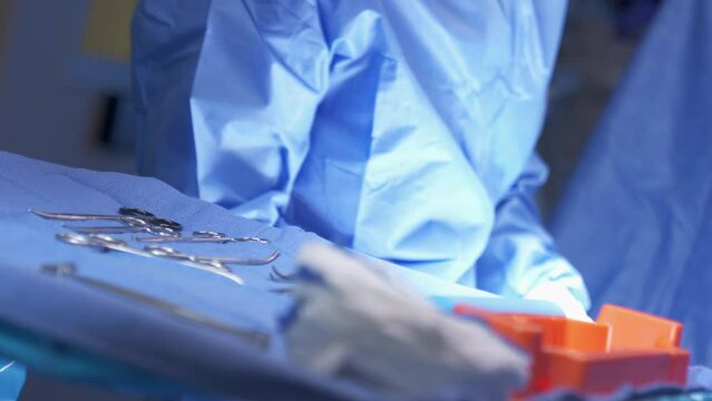 Surgical Instruments in Foreground Tray with Surgeon. sanitized surgical instruments on a tray with blue cloth for operation with surgeon in background