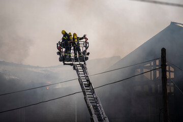 Dramatic scene of Firefighters rising on a mechanical sliding ladder crane to the epicenter of the...