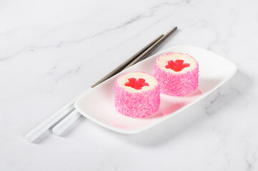 Vegan white chocolate cream cake in the form of round sushi with a jelly flower, sprinkled with coconut shavings on a serving plate. Light background