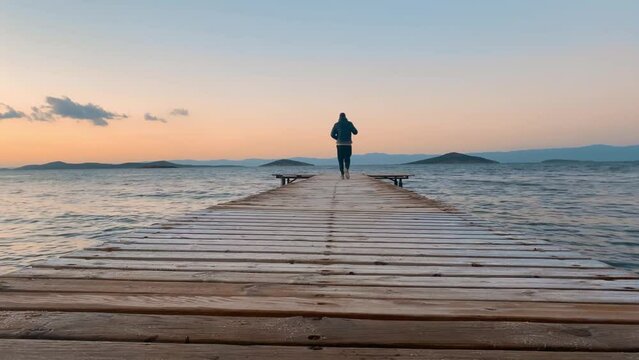 Boy walking wooden pier at colorful sunset,4K. Back shot, winter. Ayvalik,Turkey