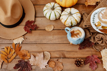 Autumn fall composition. Wooden desk table with knitted sweater, hot coffee, hat and pumpkin. Flat lay, top view. Nordic, hygge, cozy home concept