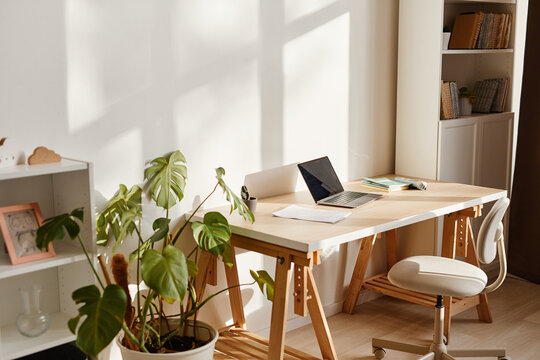 Background image of minimal home interior with laptop on desk and workplace lit by sunlight, copy space
