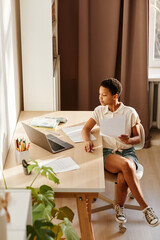 Minimal portrait of African American girl studying online in cozy home interior lit by sunlight