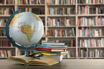 Globe, books and eyeglasses on wooden table on wooden table in library. Space for text