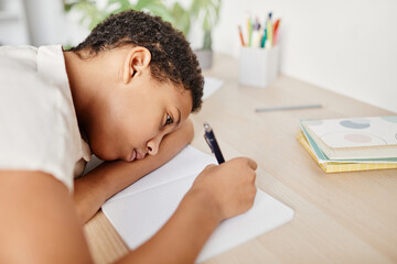 Portrait of sad and bored child laying head on desk while struggling with homework