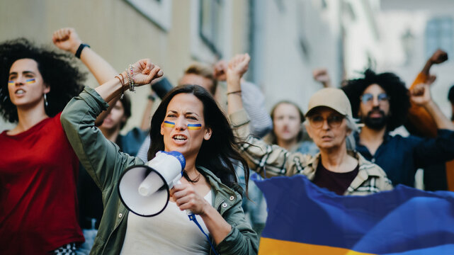 Crowd of activists protesting against Russian military invasion in Ukraine walking in street.