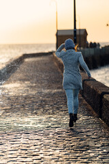 woman flees the water from a wave that has crashed against the promenade wall