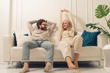 caucasian couple relaxing and stretching their arms on a sofa placed in their renovated living room. High quality photo