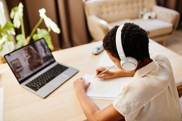 High angle portrait of African American girl watching online lesson with headphones while studying at home