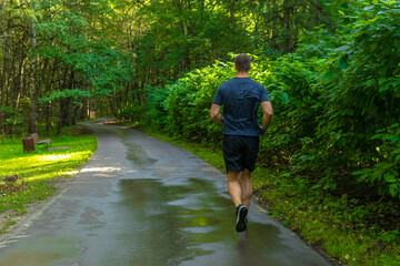 A man athlete runs in the park outdoors, around the forest, oak trees green grass young enduring athletic athlete forest, lifestyle outdoor training wellness marathon, jogging outside. Autumn body