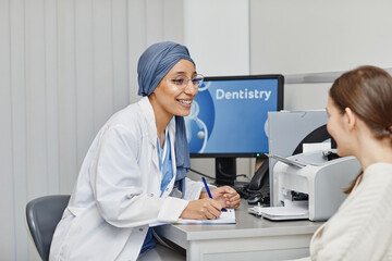 Naklejka premium Side view portrait of smiling female dentist consulting patient in office at modern dental clinic