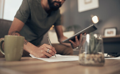 Getting his financial act together. Cropped shot of a man using a digital tablet while going through paperwork at home.