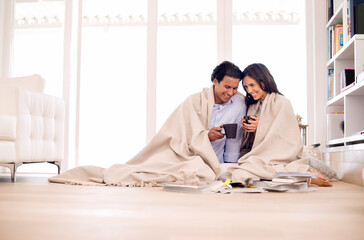 Making the most of their time together. Shot of a young couple sitting on the floor wrapped in a...