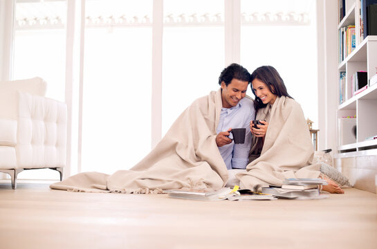 Making the most of their time together. Shot of a young couple sitting on the floor wrapped in a blanket looking at photo albums.