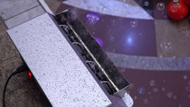 Machine for making soap bubbles. Machine blowing soap bubbles. Big bubbles are seen blowing out of an automatic black bubble machine. 