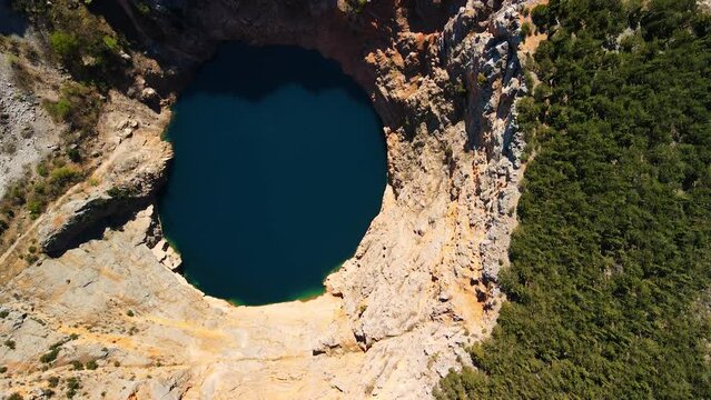 Flying over the Red Lake containing a karst lake close to Imotski, Croatia. The largest collapse doline in Europe with high cliffs. The picturesque sight of the greatest landscape diversity 4K UHD