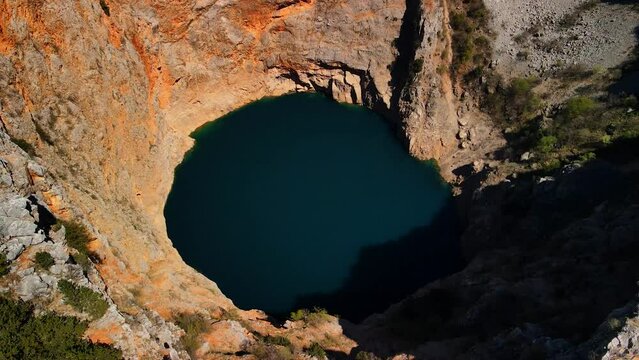 A drone shot of Red Lake or Crveno jezero which is a collapsed sinkhole containing a karst lake close to Imotski, Croatia. It is 530 meters deep, thus it is the largest limestone crater in Europe.