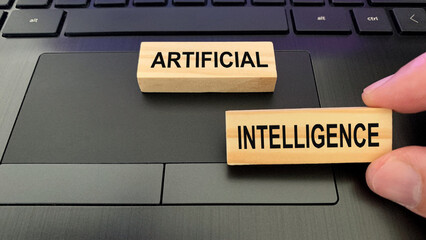 Artificial intelligence text on wooden blocks with laptop background.