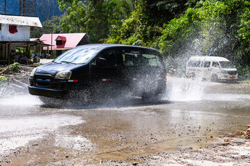 A mid-size van in puddles, mud and splashes. The Peruvian jungle in the background