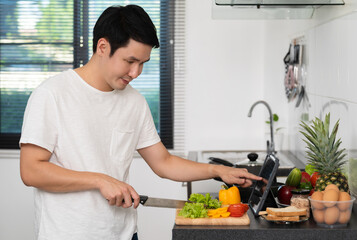 man cooking and preparing vegetables according to a recipe on a tablet computer in kitchen at home