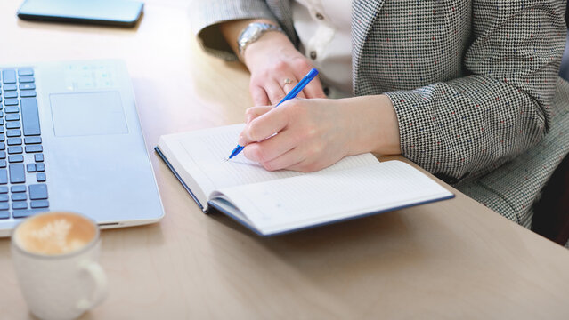 woman in formal clothes making notes in a diary. left handed person. international left handers day. crop view.