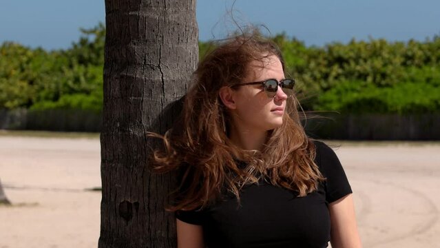 Young woman leaning against a palm tree at Miami Beach